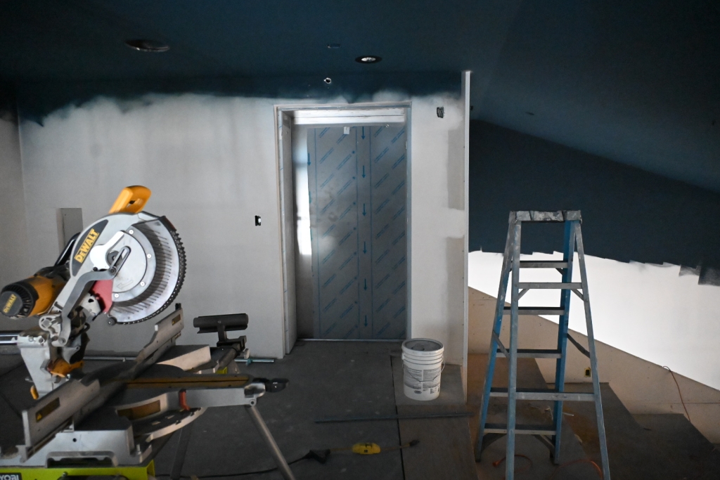 Painting has begun at Johnson Hall in Gardiner, Maine. Photo shows construction equipment inside the building and a dark blue green paint on the top half of the wall near the elevator.